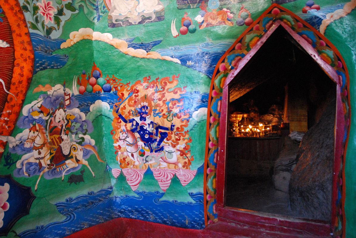 34 Entrance To The Cave Of The Female Yak Horns At The Back Of Dirapuk Gompa On Mount Kailash Outer Kora A small opening at the back of the Dirapuk Gompa leads to the slanted rood of the cave of the female yak horns. I�m not sure who the figure is to the left. He is white with one face and two hands holding upraised in the right a riding whip and in the left a spear with a red banner. The final figure to the lower right is Shri Devi (Tib. Palden Lhamo), dark blue in colour, riding side saddle on a white mule with a sword in her upper right, a skullcup in her lower right, and khatvanga in her first right hand and another staff in her far right hand. She has a sun and moon disc at her waist.